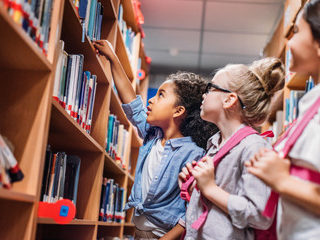 Three young girls looking at books on shelf in library.