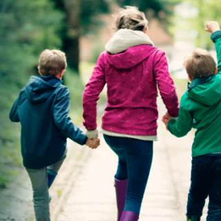 two children and parent walk down sidewalk