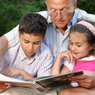 Grandfather reading to two young grandchildren outside