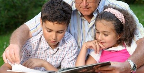 Grandfather reading to two young grandchildren outside