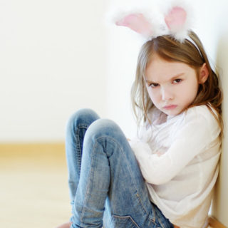 Young girl sitting with arms crossed and mad face while wearing rabbit ears