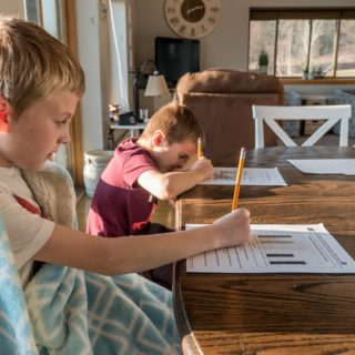 Two young boys working on school worksheets with pencils on a kitchen table