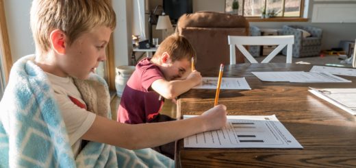 Two young boys working on school worksheets with pencils on a kitchen table