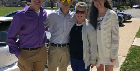 Grandma with three high school aged kids standing outside on a sunny day smiling and looking at the camera.