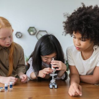 Three girls in first grade taking turns looking in a microscope