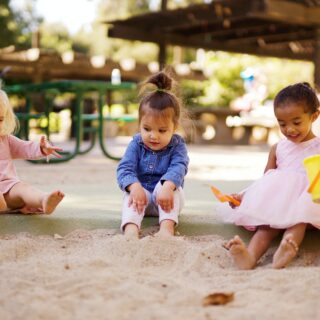 Three toddlers playing in the sand together