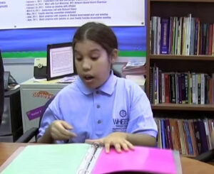 A student seated at a school desk with an open binder