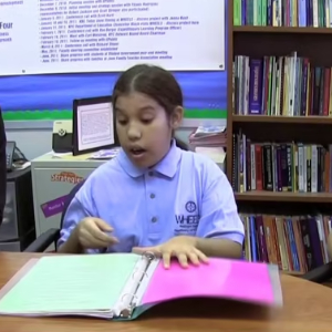 A student seated at a school desk with an open binder