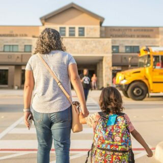 adult walking with young child in front of a school