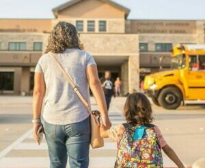 adult walking with young child in front of a school