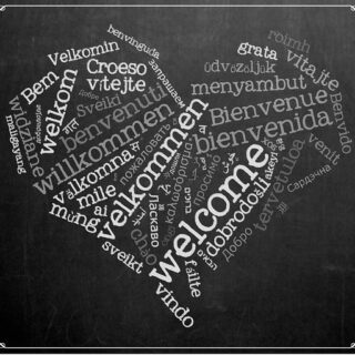 welcome written in many languages in chalk in a heart shape
