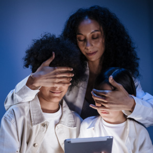 mother shielding her 2 kids eyes from the light of a tablet